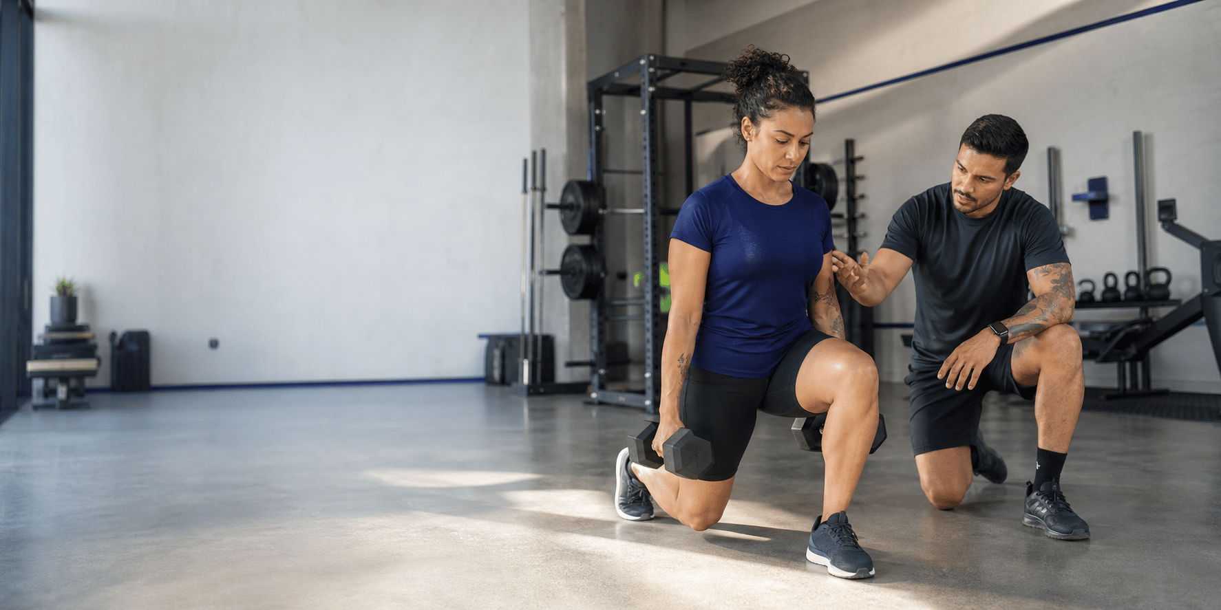 Personal orientando uma aluna durante um exercício com halteres